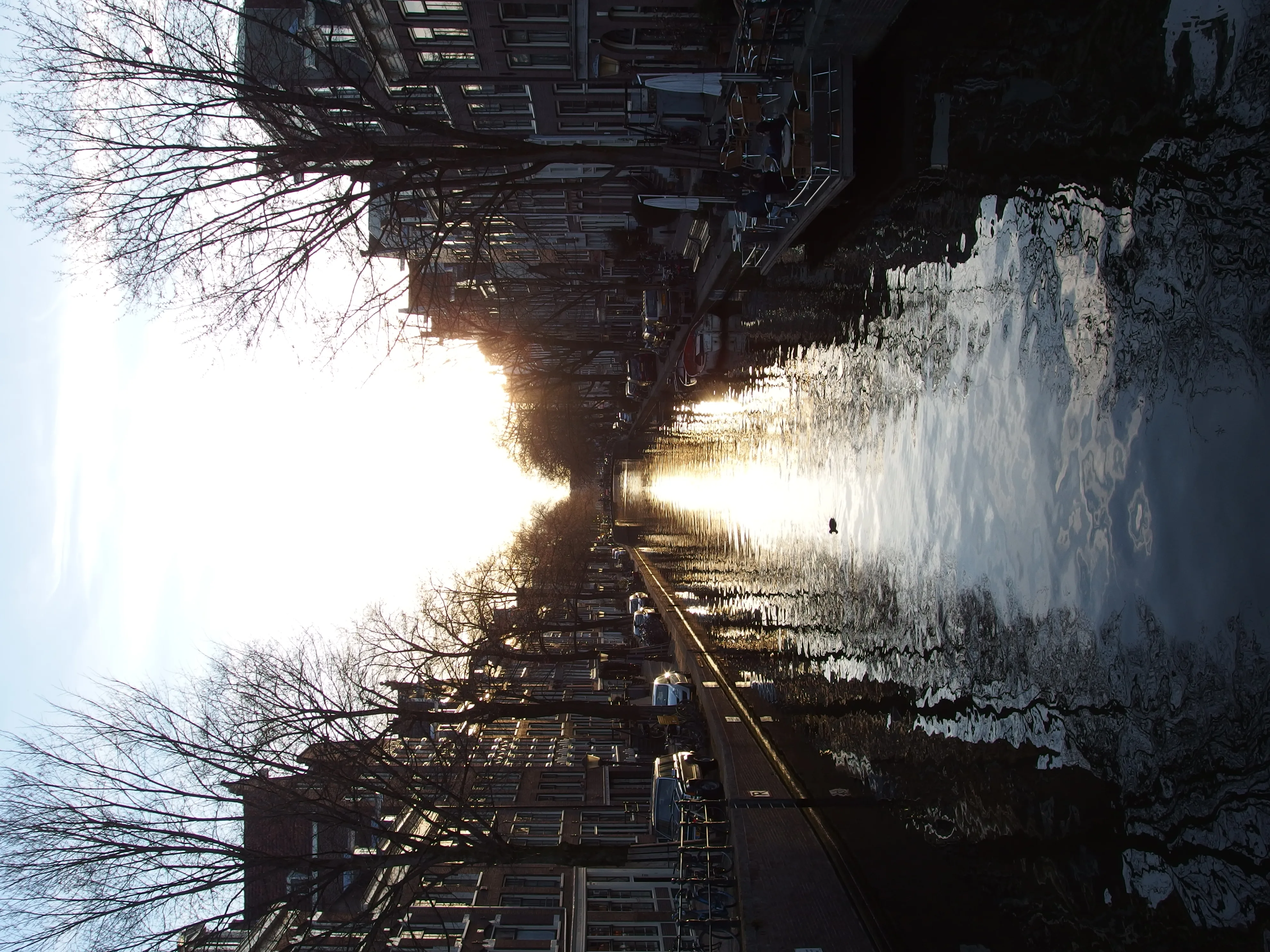 Een gracht in de Jordaan bij zonsondergang, met grachtenpanden en bomen weerspiegeld in het water